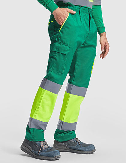 Groene werkbroek met fluorescerend gele en grijze reflecterende stroken, voorzien van zijzakken en gedragen met veiligheidsschoenen.