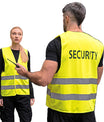 Twee beveiligingsmedewerkers dragen gele veiligheidsvesten met reflecterende strepen en het opschrift ‘Security’, in een industriële omgeving.