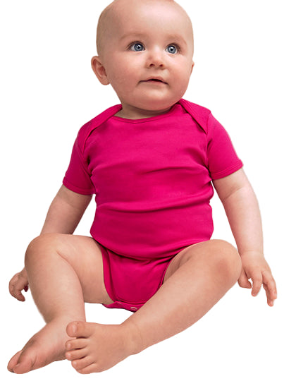 baby in een felroze romper tegen een volledig witte achtergrond, zittend en omhoog kijkend